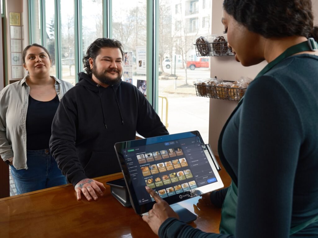 Barista using POS system to serve two customers at a café counter, showcasing modern restaurant technology.
